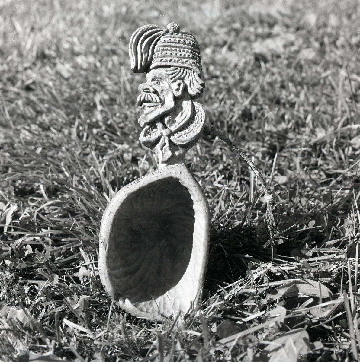 En kåsa med skaft i form av ett manshuvud, stående på en gräsmatta.
