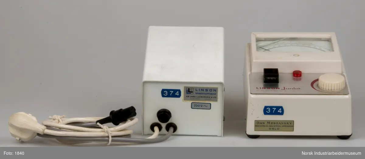 Måleinstrument med analog viser og tilhørende transformator. Instrumentet er et fotometer for hemoglobinundersøgelser og kan måle mængden af lys der trænger gennem en væske. Transformatoren er en 220 volt enhed og er forsynet med en ledning isoleret med blød plast.