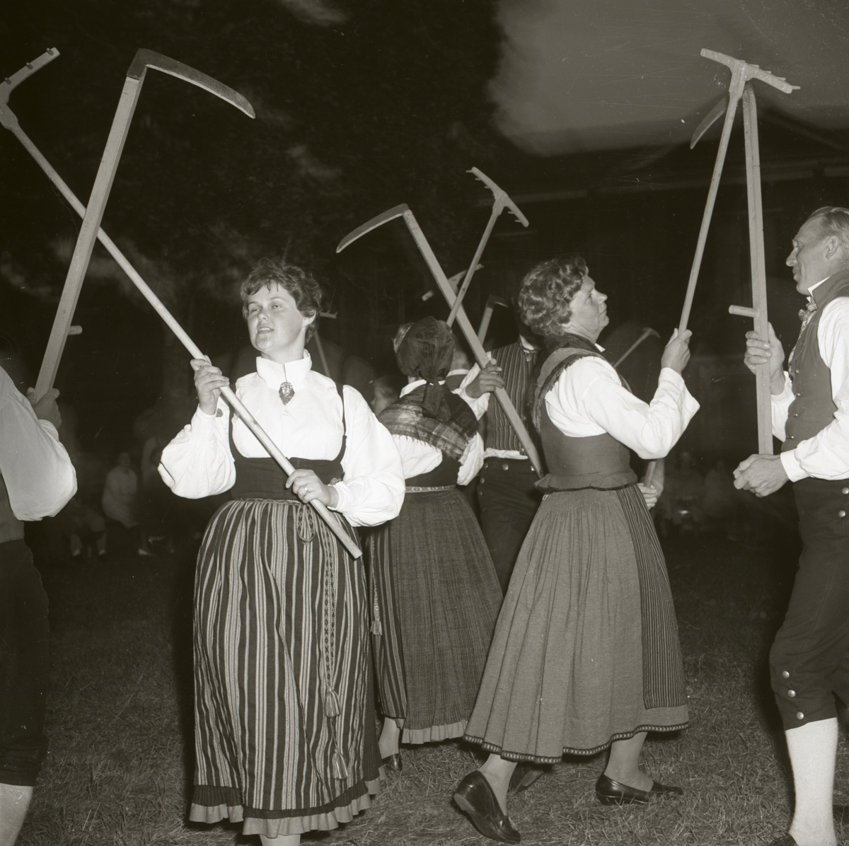 Danslaget genomför en dans där de håller upp varsin lie eller kratta. De är iklädda folkdräkter, 1962 i Rengsjö.