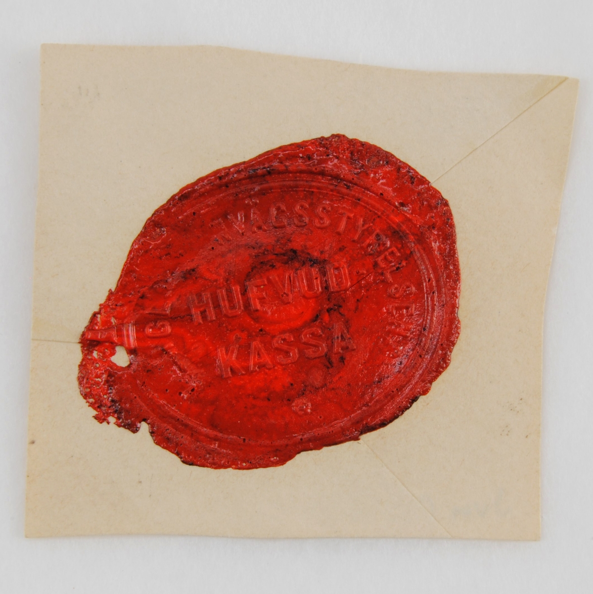 Ovalt sigillavtryck i rött lack på gultonat kuvertpapper. Text finns både längs kanten och i rader mitt på sigillet. Underst finns en liten blomma.