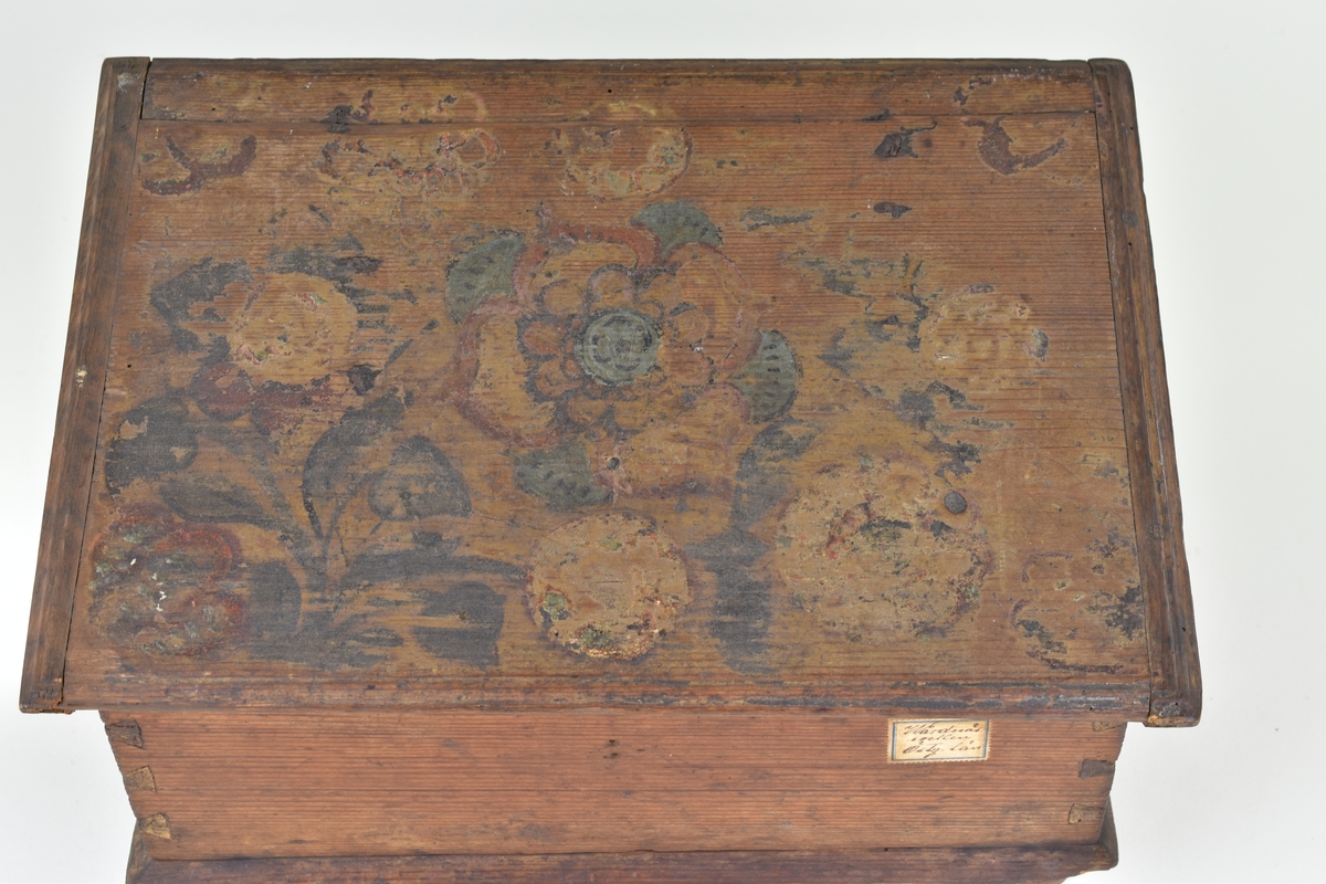 Skrin av furu med pulpetlock och inredning med fack och låda. På utsidan brunmålat och blomstermotiv på locket. På lockets insida bemålat med årtalet 1766 inom en krans.