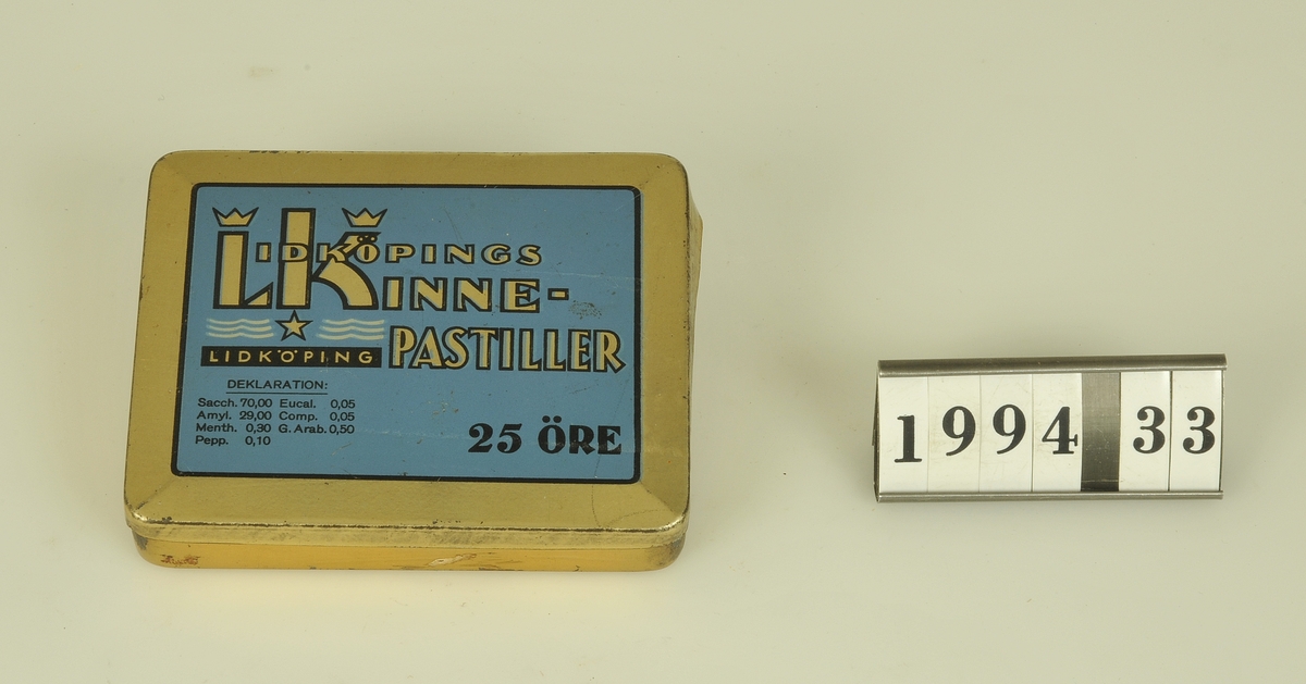 Pastillask av bleckplåt i guld med blått tryck ”Lidköpings Kinnepastiller”. Pastillerna tillverkades ursprungligen av Lidköpings Konfektindustri (LK), grundat 1932. Efter ett ägarbyte 1935 kom företaget att bli en del av bolaget Kinnevik som då nyligen också köpt upp Suchard i Alingsås. 1938 slog man ihop de båda företagens produktioner och LK flyttade sin verksamhet hit till Alingsås.