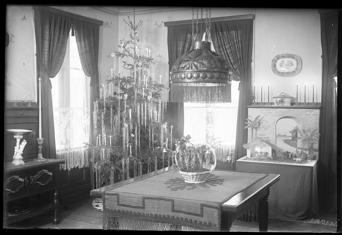 En interiörbild på ett julpyntat finrum. I ena hörnet står en julgran klädd med glitter och ljus. I fotografens anteckningar står det "Interiör Segerfors"
