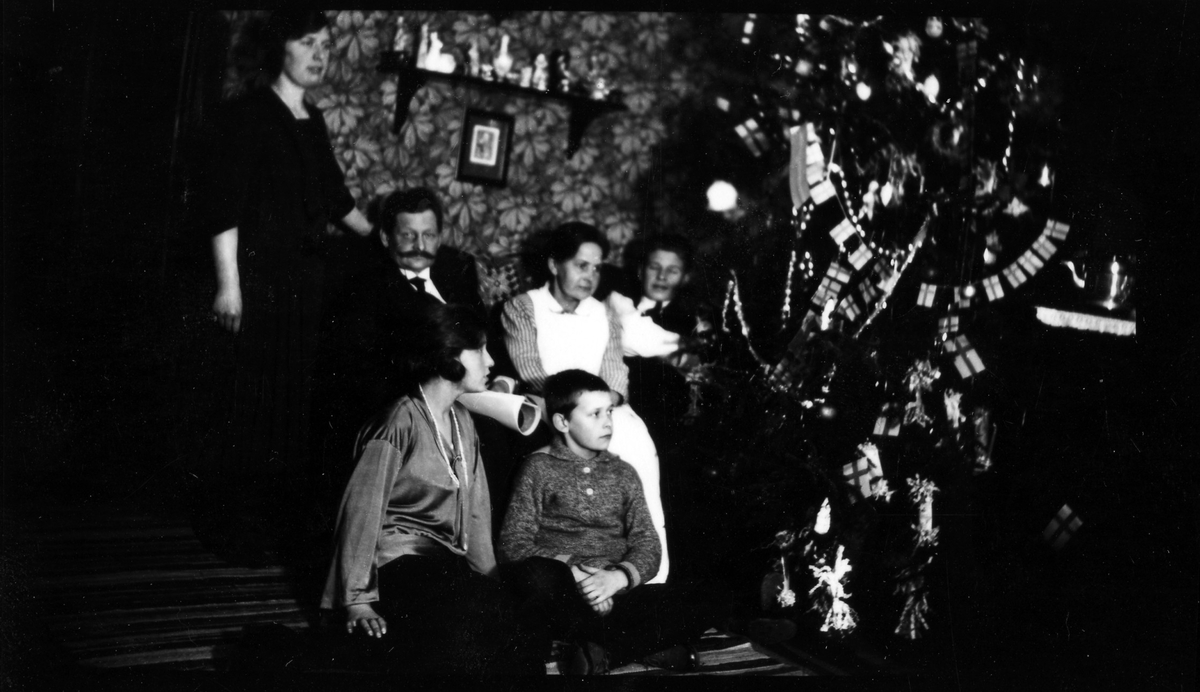 En familj sitter vid sin pyntade julgran, två av barnen sitter på golvet.