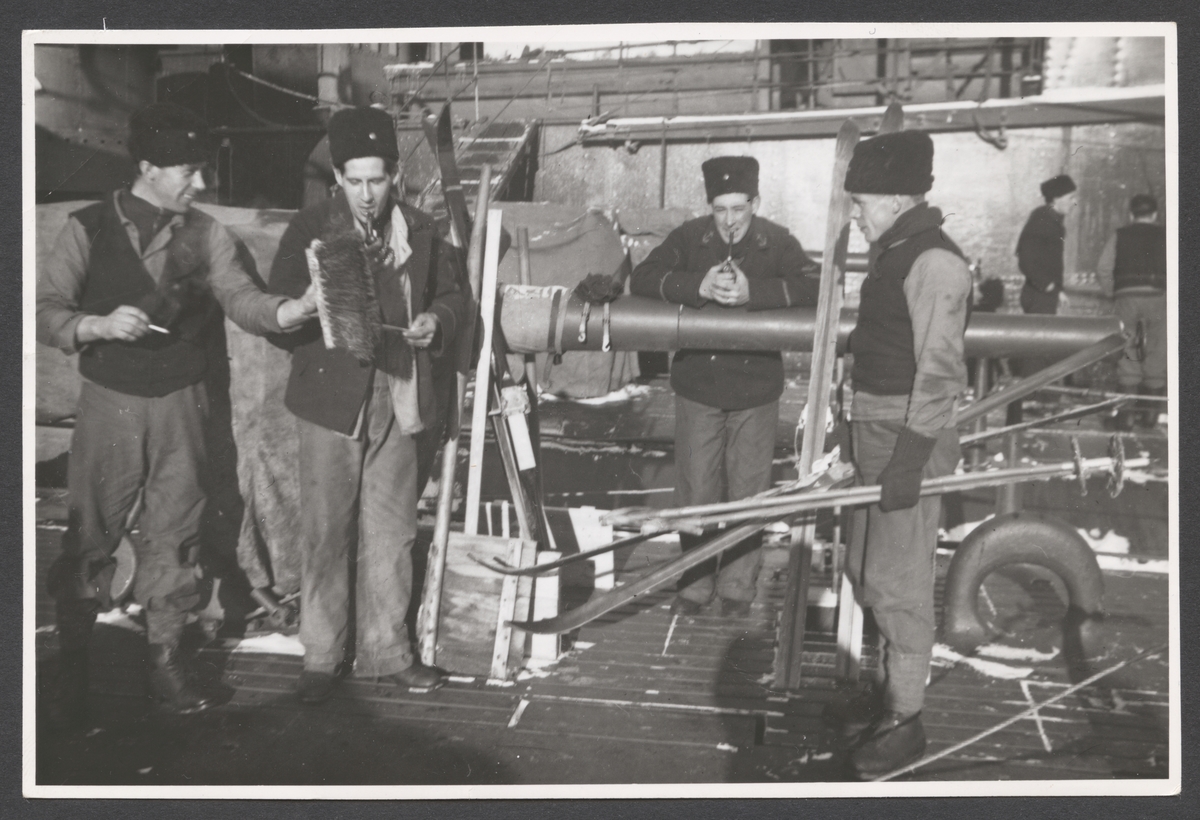 Bilden visar en grupp besättningsmän på däck av ett örlogsfartyg som verka har fritid. Stämningen bland de fyra unga män är avslappnad. I centrum står förmodligen Evert Ingemansson som stödjer sig på ett eldrör och röker pipa. På hans höger sida syns två kamrater som också röker och verka göra en skämt med en kvast. Fjärde mannen på Ingemanssons vänster sida är på väg att åker skidor. All fyra bär arbetskläder och vintermössor.