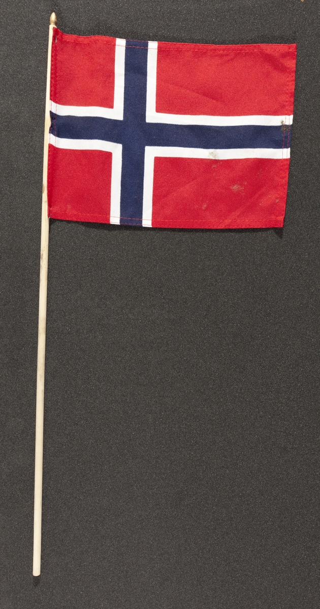 Flagg innsamlet etter terrorhandlingen 22. juli 2011 fra minnesmarkeringene i Lillestrøm. 

Klassisk norsk flagg slik vi kjenner det fra 17.mai feiringer: Blått kors i midten, hvitt kors som "omkranser" det blå (litt tynnere fargefelt) på en rød bakgrunn, de blå og hvite korsene går helt til kanten av flagget. Dimensjonene på feltene er slik at de to røde felten mot pinnen er halvparten så store som de to ytterste røde feltene. Flagget brukes av både barn og voksne.Tuppen på pinnen som flagget er stiftet på er malt med gullfarge. Pinnen og flagget er blitt litt misfarget av opphold utendørs. Sømmene på flagget er røde.
