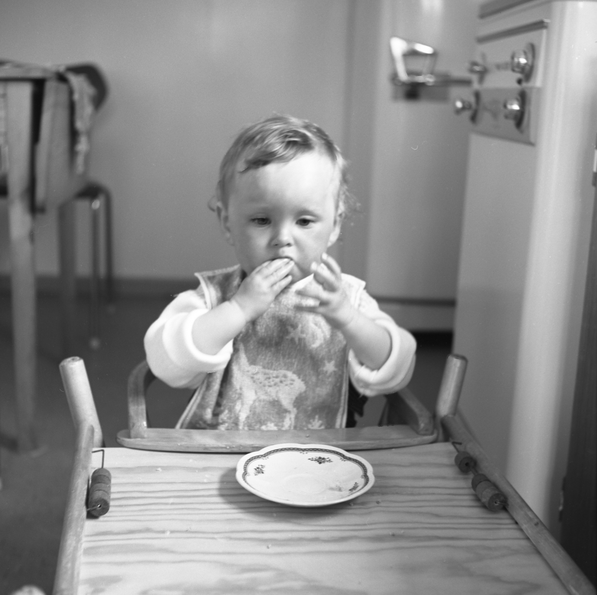 Portrettfotografi i serie av ei lita jente, Astri, som sitter i en barnestol og spiser kveldsmat.