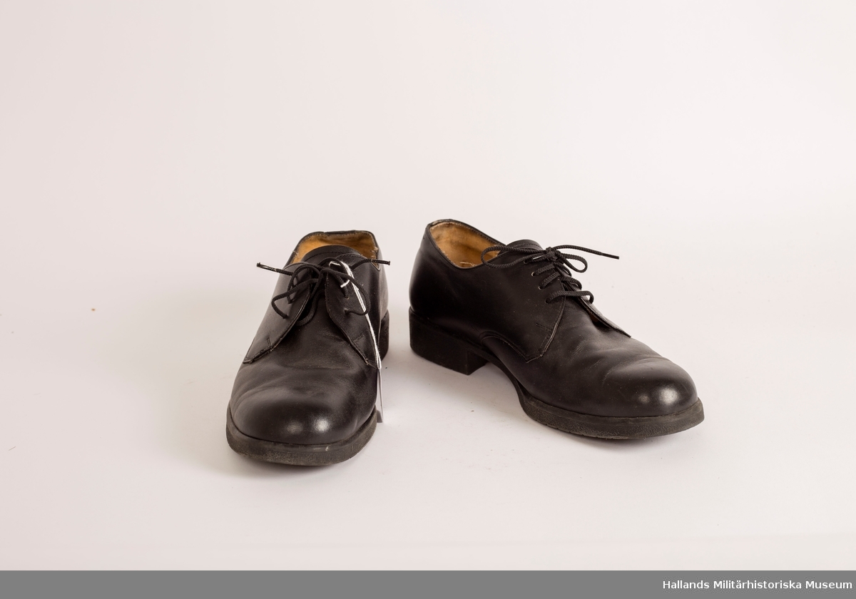 Ett par svarta lågskor, i läder med utanpåliggande raksömmar. Svarta gummisulor. Snörning på ovansidan av skorna med tunna svarta textilsnören. Hålprägling på plösen: 44 H. På innersulorna bär skorna kronstämpeln samt är märkta: 44 H, A & O. Skorna är märkta på insidan, höger kant med vit stämpel: 44 H833519 7 D.
