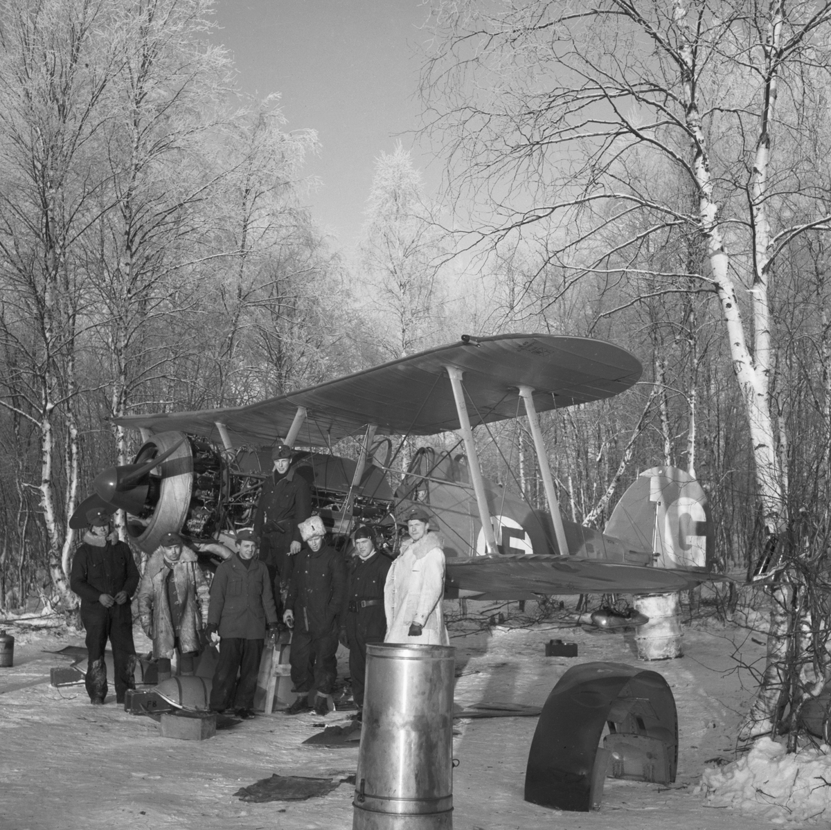 Gruppbild av militärer vid flygplan Gloster Gladiator märkt gul G under demontering efter Finska vinterkrigets slut i mars 1940 vid Svenska frivilligkåren i Finland, F 19.