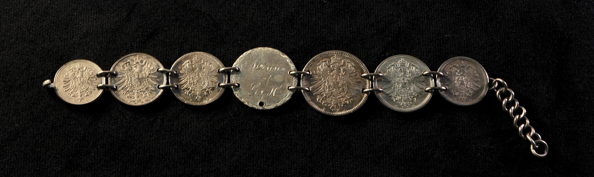 Beskrivning: Ett st. armband, bestående av sju st. tyska och spanska mynt från 1870-talet. På det spanska myntets baksida är ingraverat: "Minne af G & H".