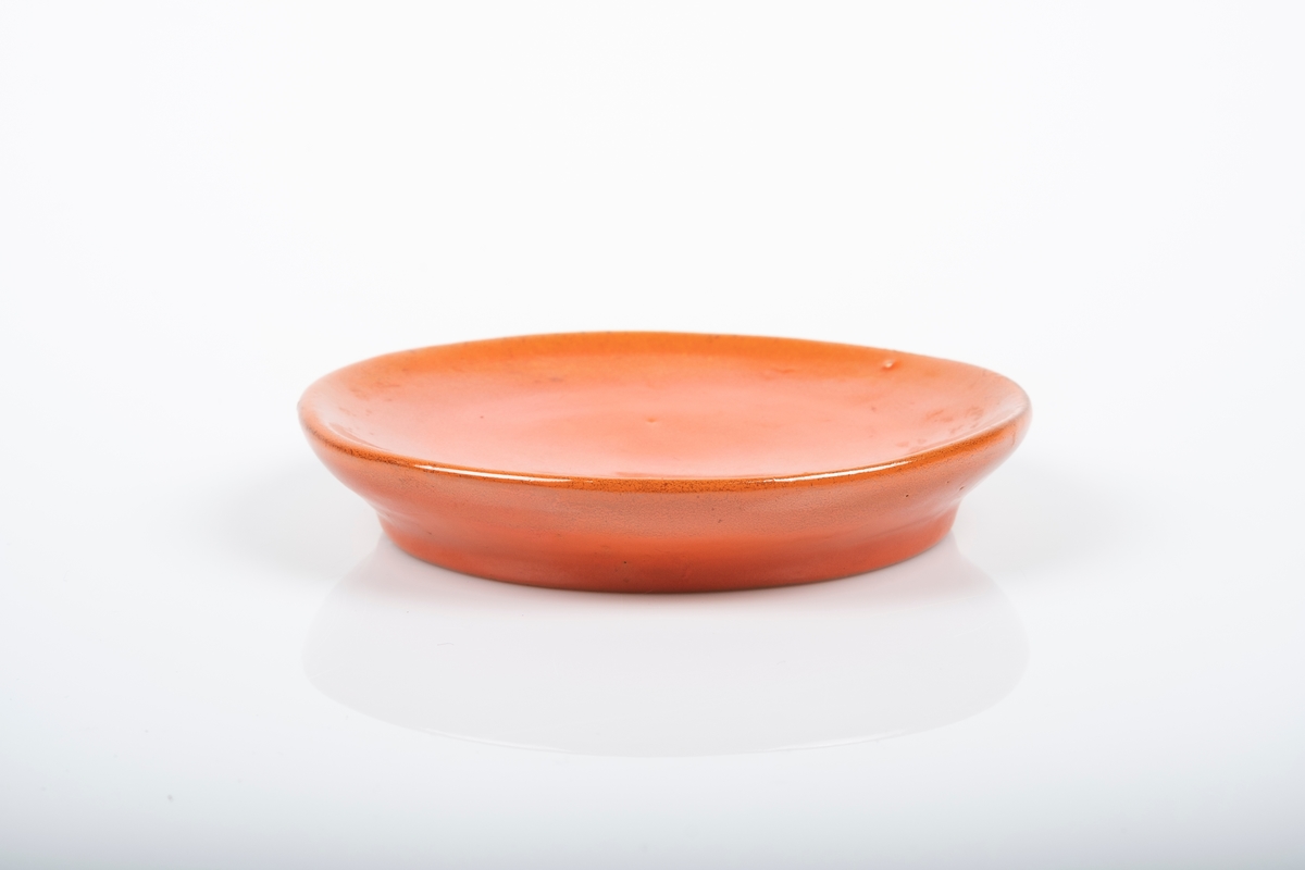 Liten keramikkskål med rød glasur. Det er innskrift på undersiden av skålen.