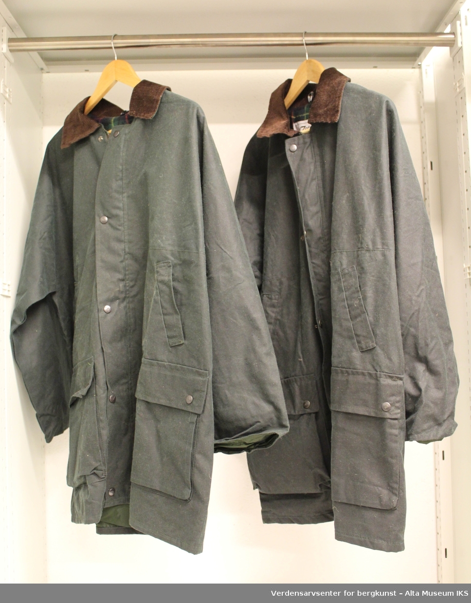 To jakker laget i oilskin, en damemodell og en herremodell. Innvendig foring er rutet, og jakkene har kraver i ribbestoff.