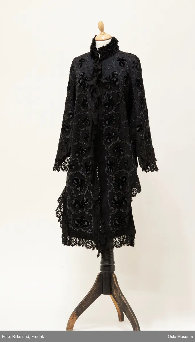 Halvlang jakkecape til å ha over kjole med kø, ca 1875
Dekor: Perlebroderi med applikasjon i fløyel kantet med maskinblonde
Størrelse: 40
Produsent: utenlandsk