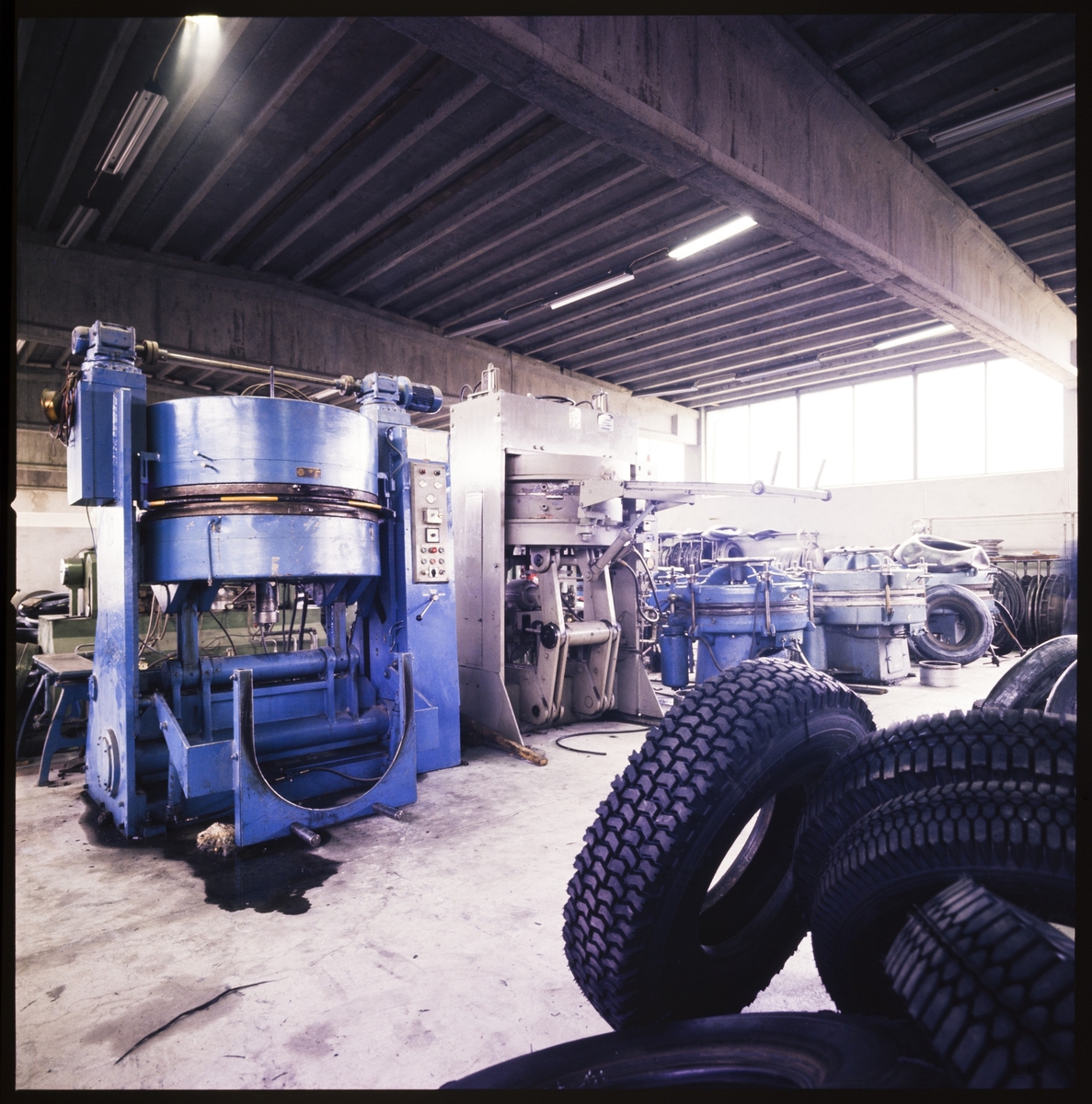 Produksjonslokalene til "Bergs gummi-industri". Det er ulike maskiner rundt om i lokalet og stabler med bildekk.