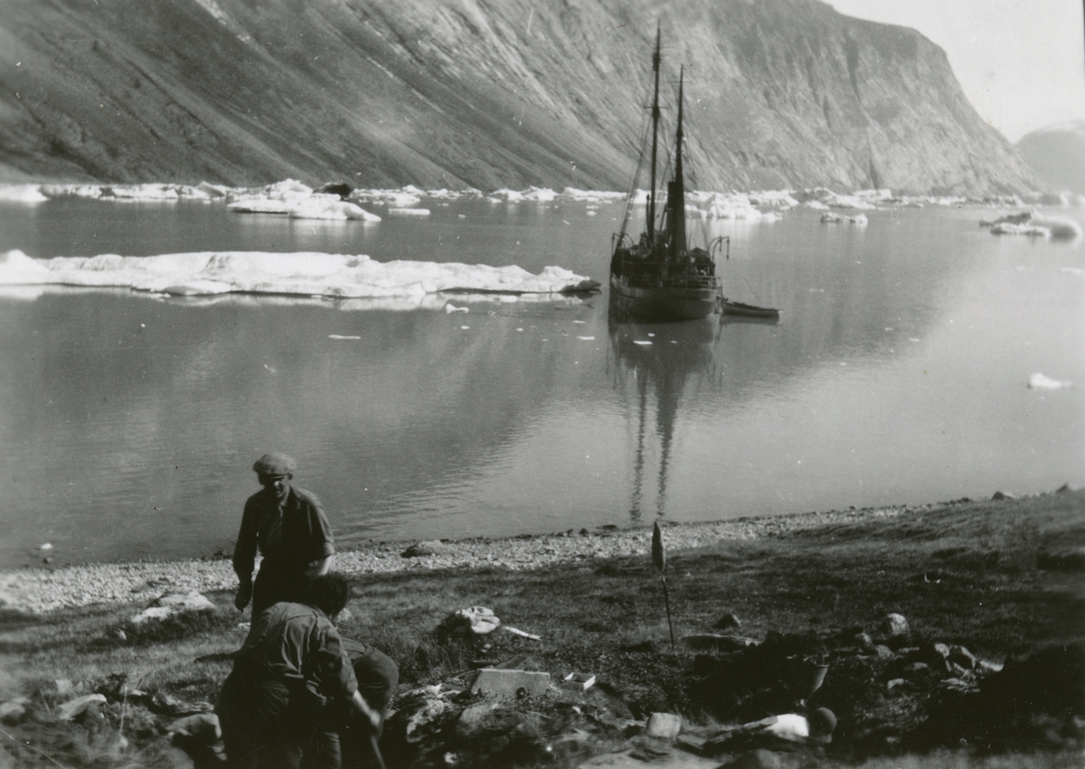 Ingvald Skjeldrup gjør utgravinger av et eskimohus sammen med en annen i Reinbukten, Isfjorden på Grønland. Båten Veslekari viser i bakgrunnen.