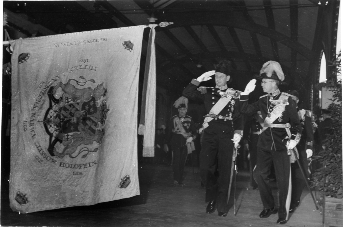 Fredrik IX av Dannmark och kronprins Gustav VI Adolf gör honnör inför Svea livgardes fana.