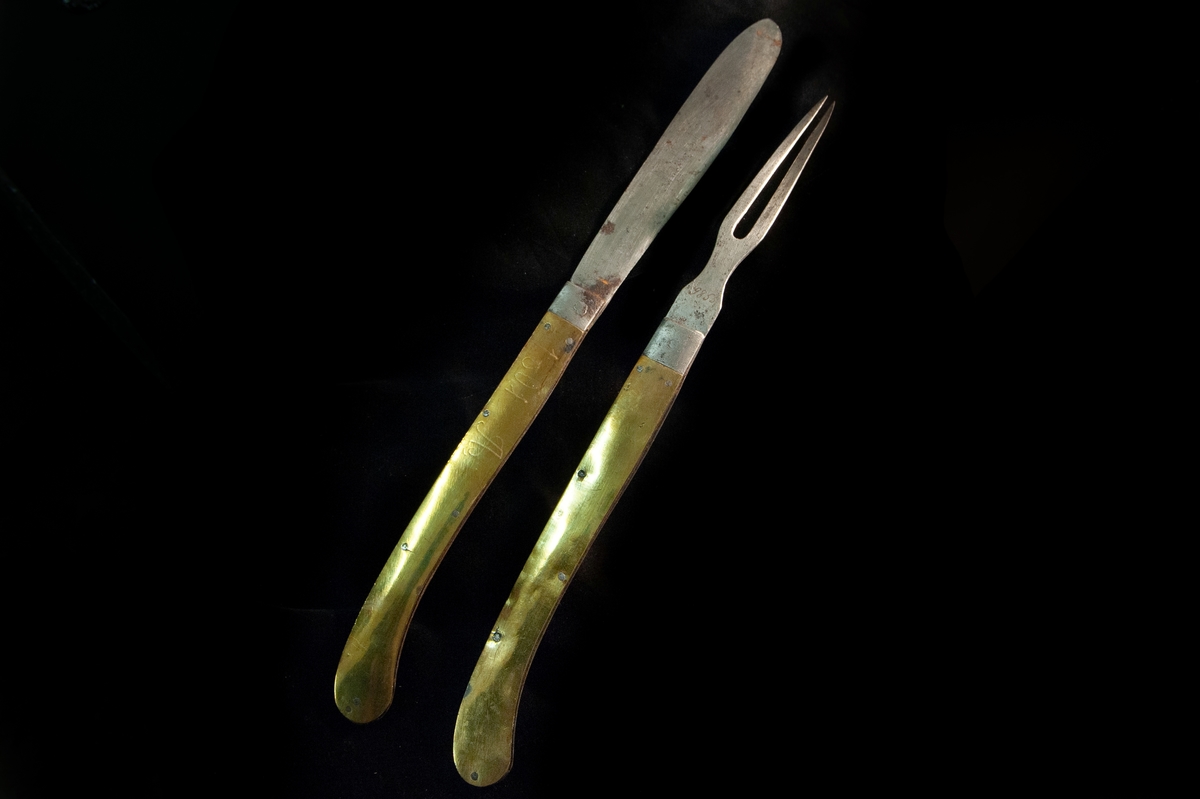 Större kniv i fällknivsmodell i järn och mässingshandtag, del i ett set med JM.09855. Benämns som "gästabudstyg" i orginalkatalog.
Graverat "1801 A" på ena sidan, och "SMD" på andra. Stämplar saknas.