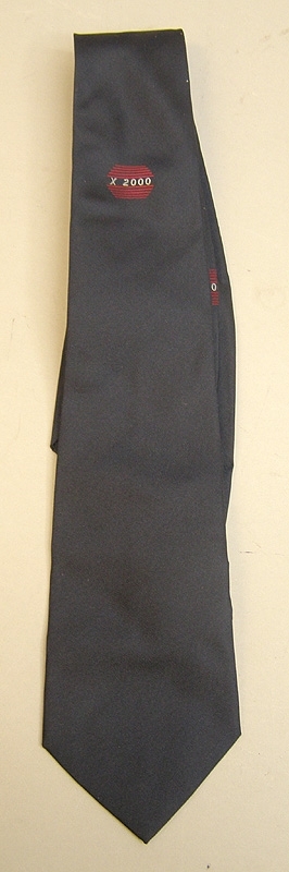 Mörkblå sidenslips på mitten framtill röda ränder ovanför och nedanför "X2000". Samma logotyp förekommer på flera ytterligare ställen på slipsen men som inte syns då man bär den. På tillverkarlapp står: "Made in Italy. 100 % seta".