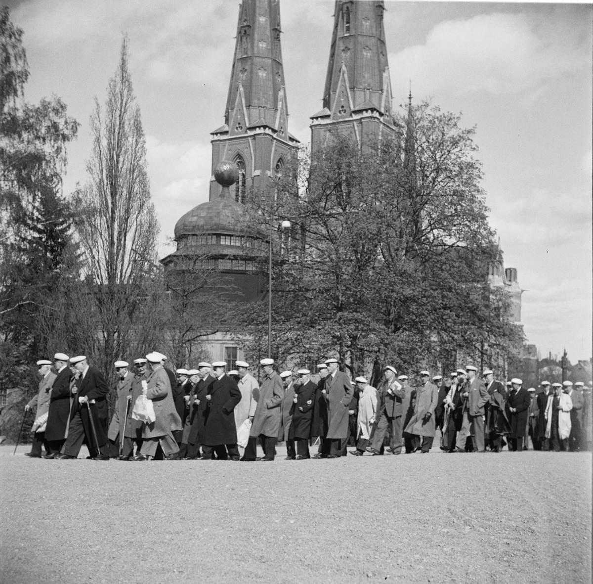 Flera personer iförda studentmössor tågar i Universitetsparken, Östgöta nations minneslandskap, Uppsala 1949