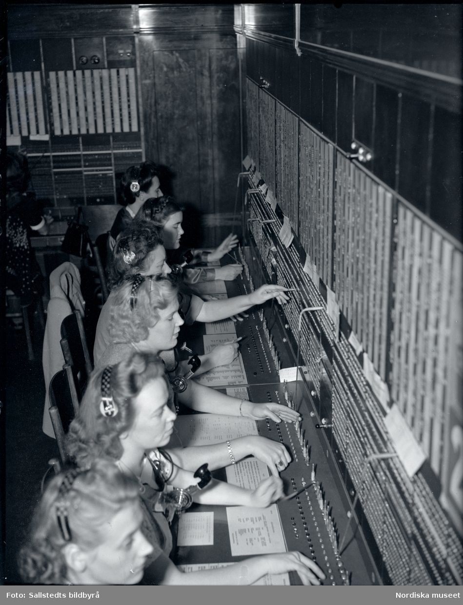 Telefonister på Stockholms telefonstation år 1946. En rad med kvinnor sitter vid ett växelbord, en snörväxel, och kopplar samtal.