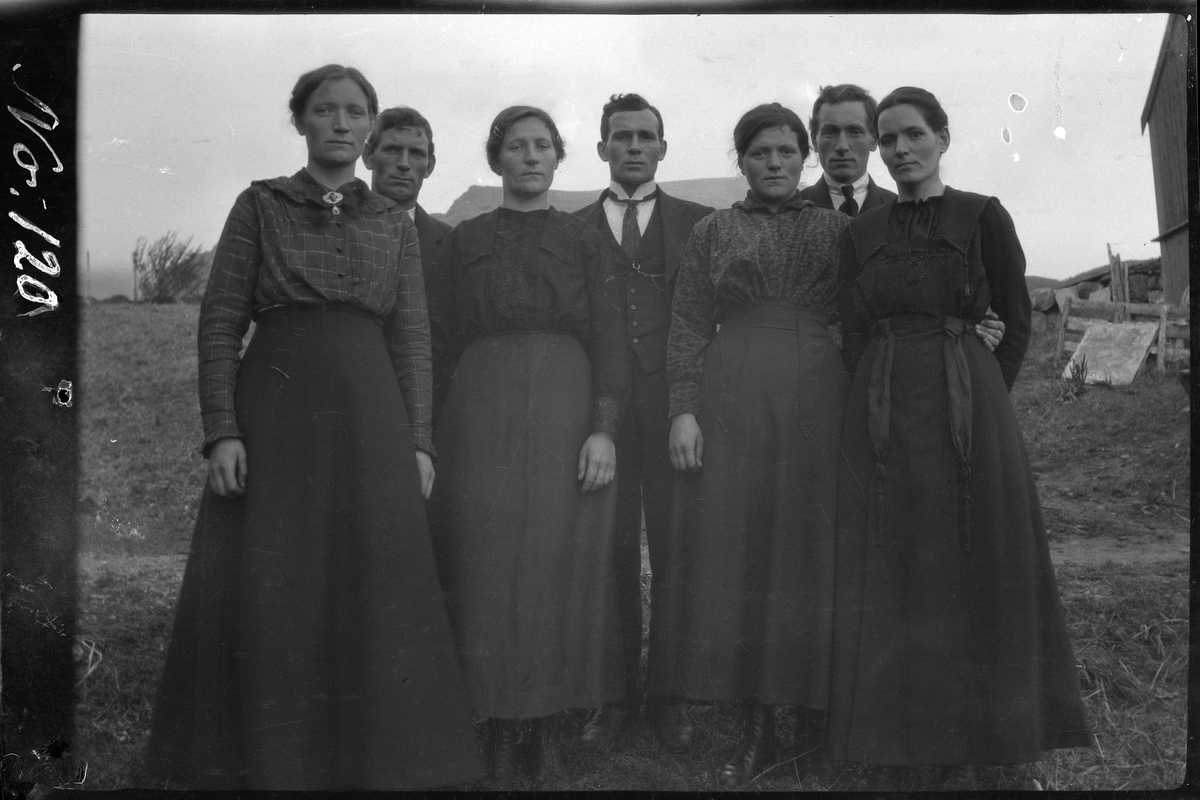 Gruppeportrett av syv personer stående på gårdstun.