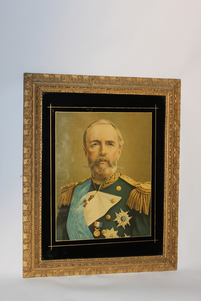 Oljetryck, litografiskt tryck med fernissad yta. Inom glas och med förgylld ram och svart passepartout. Föreställande kung Oscar II (1829-1907) i uniform. Den förgyllda ramen har Sveriges vapen inpräglat med jämna mellanrum runt hela ramen.