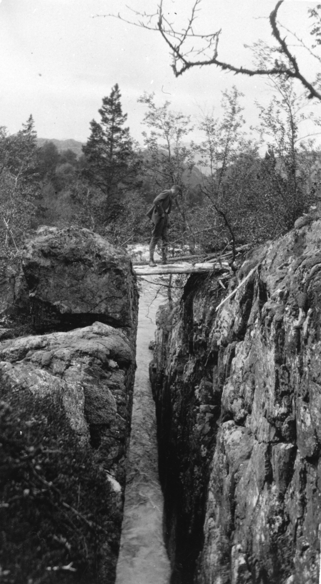 En mann står på noen trestammer som ligger over Mostøljuvet ovenfor Mosvatnet i Suldal.