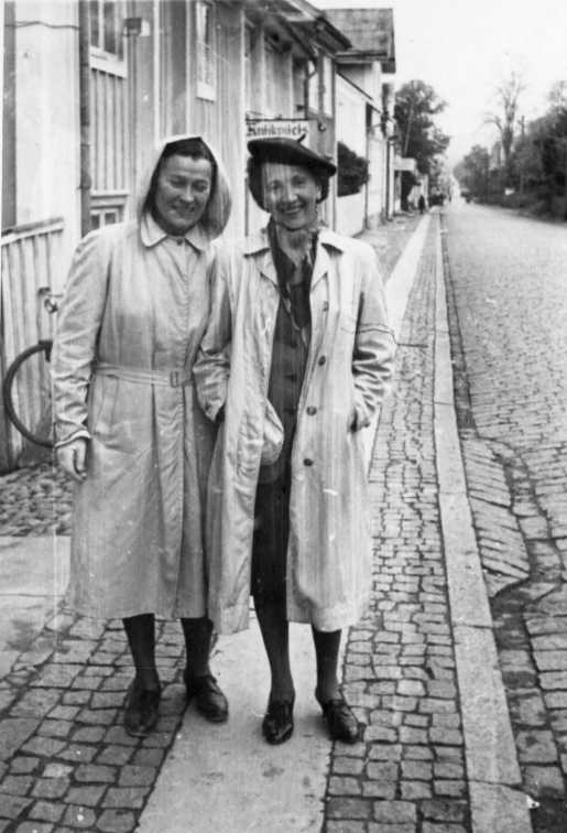 Två kvinnor i ljusa kappor står utanför Brahegatan 7. Kvinnan till vänster är möjligen Elsa Ekwall som bor i grannhuset.