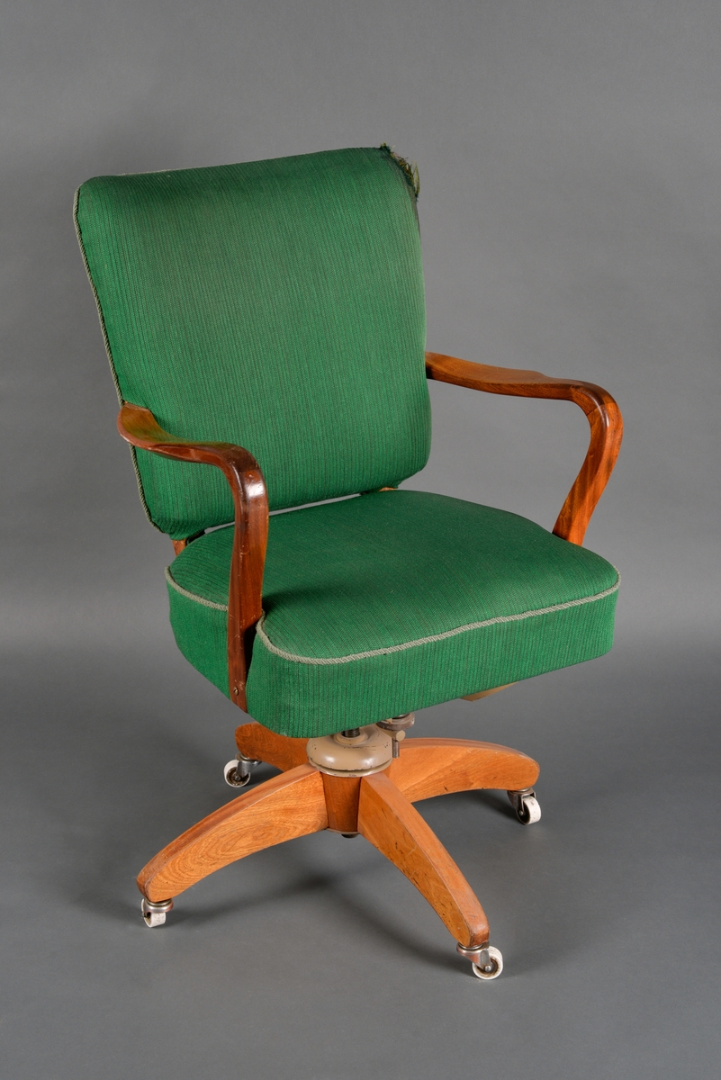 En dreibar kontorstol med armlener. Stolen er laget av heltre, huntonittplate og stålrørkonstruksjon. Den har sammenføyninger med skruer og lim samt treforbindelser. Det er grønt tekstil på sete og rygg. Langs kanten på setet er det grått pyntebånd (possement). Både sete og rygg er firkantet og har polstring bestående av farget ullblanding og skumplast. I setet er det metallfjærer. Stolen har fire bein med hjul på. Både treverket og metallet er lakkert.