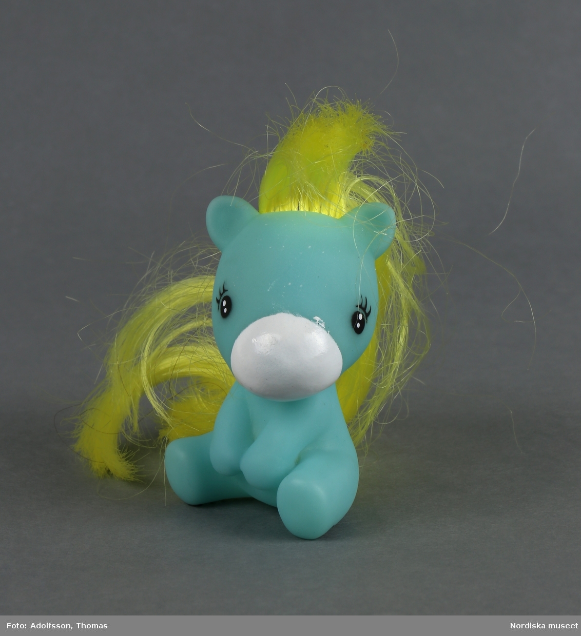 Sittande leksakshäst som kallas My Little Pony. Turkos kropp, vit nos och gul man av syntethår som går att kamma. Påmålade svarta ögon och ögonfransar.