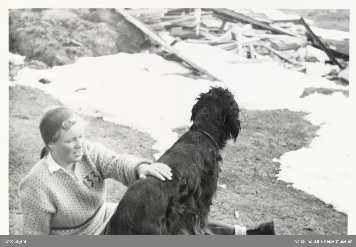 Jente med pannebånd sitter med hund på gressflekk ved snøen