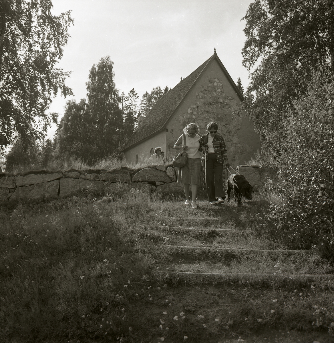 Två personer på promenad vid en gammal kyrka i Högsjö, Ångermanland 1974.
