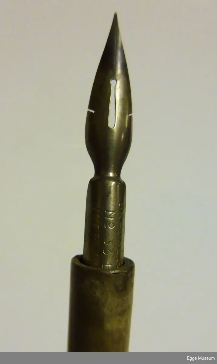 Dekorert penneskaft i metall med pennesplitt. Skaftet er smalt i enden og blir gradvis tykkere nærmere splitten.