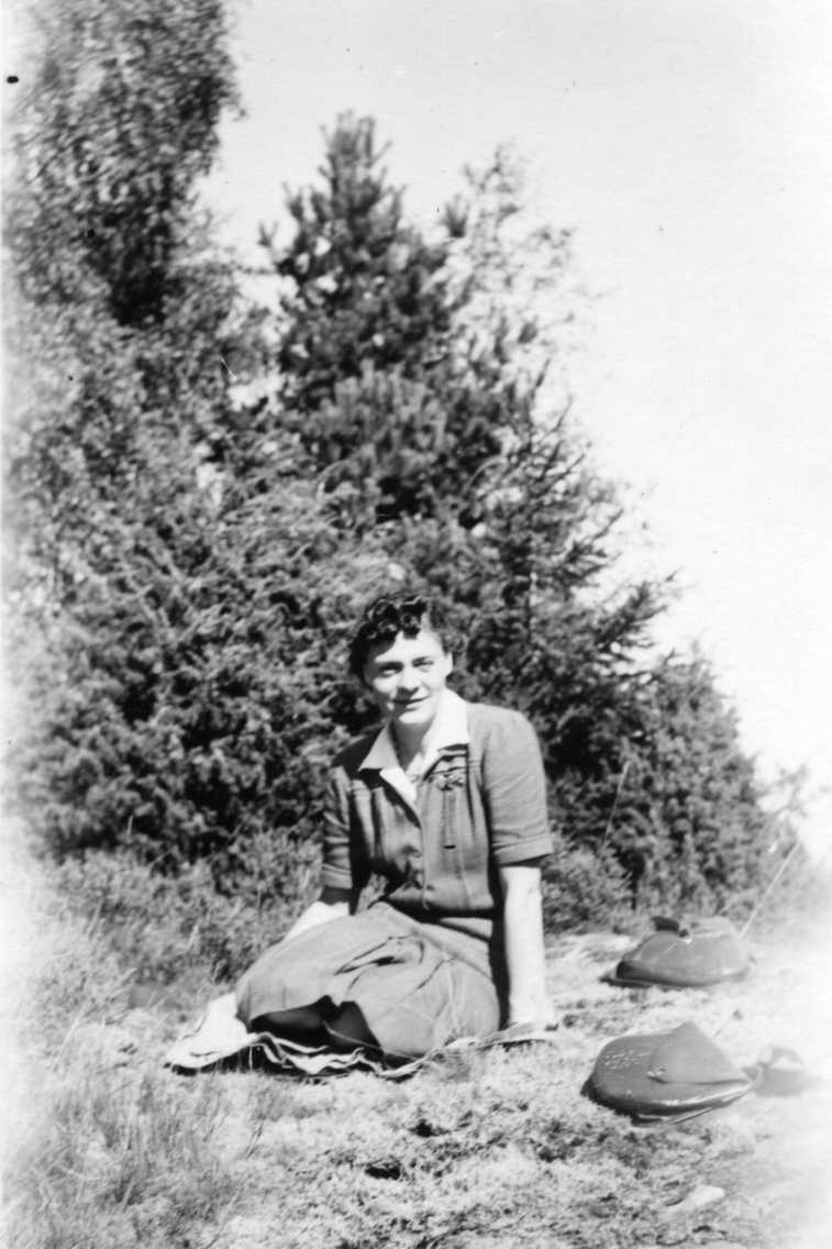 En kvinna, Nyqvist från Åsa, sitter på marken vid en skogsglänta.