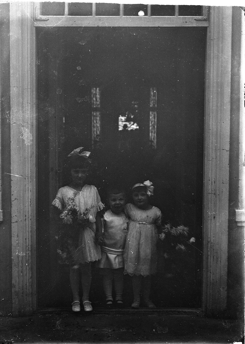 Två små flickor med en liten pojk emellan sig. De är klädda i ljus och flickorna håller en blomsterbukett i handen. De står sannolikt vid entrén till Ribbagården. Flickorna är möjligen Margit och Birgit von Otter.
