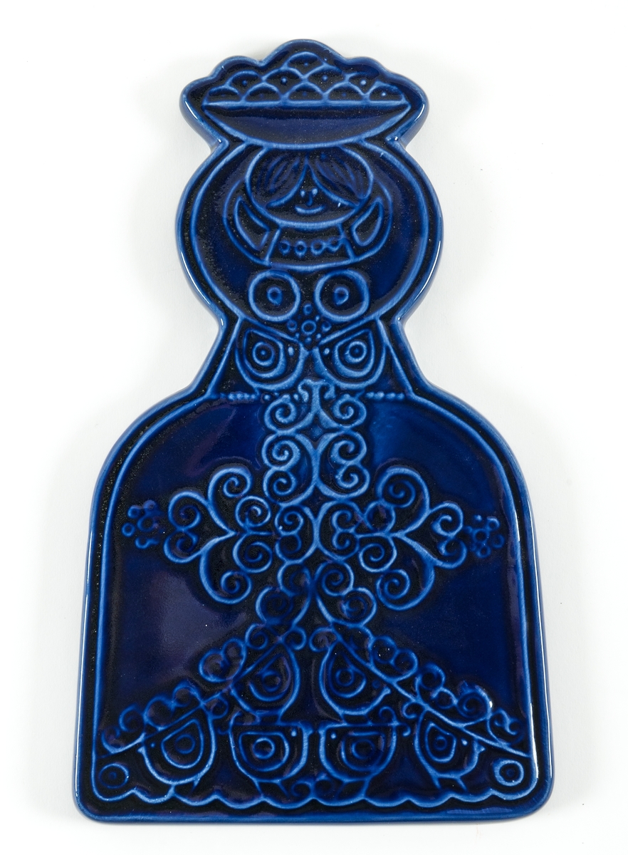 Relieffigur i blåglaserad flintgods från Steninge Lervarufabrik. Figuren föreställer en kvinna. Blomdekor på hennes dräkt. Troligen tänkt som väggdekoration. Troligen tillverkad under perioden 1960-1980 pga stilen. Bildar ett par tillsammans med relieffigur föreställande en man GM41872.