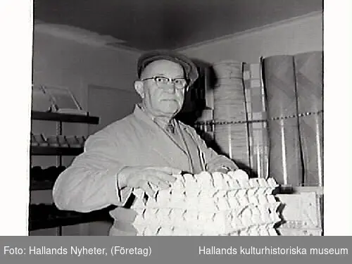 John Johansson står vid en trave ägg i Konsum Frillesås. I bakgrunden står rullar med vad som kan vara prover på olika linoleummattor.
Bild 2 visar John med en i papp inslagen sockerpaket på axeln.