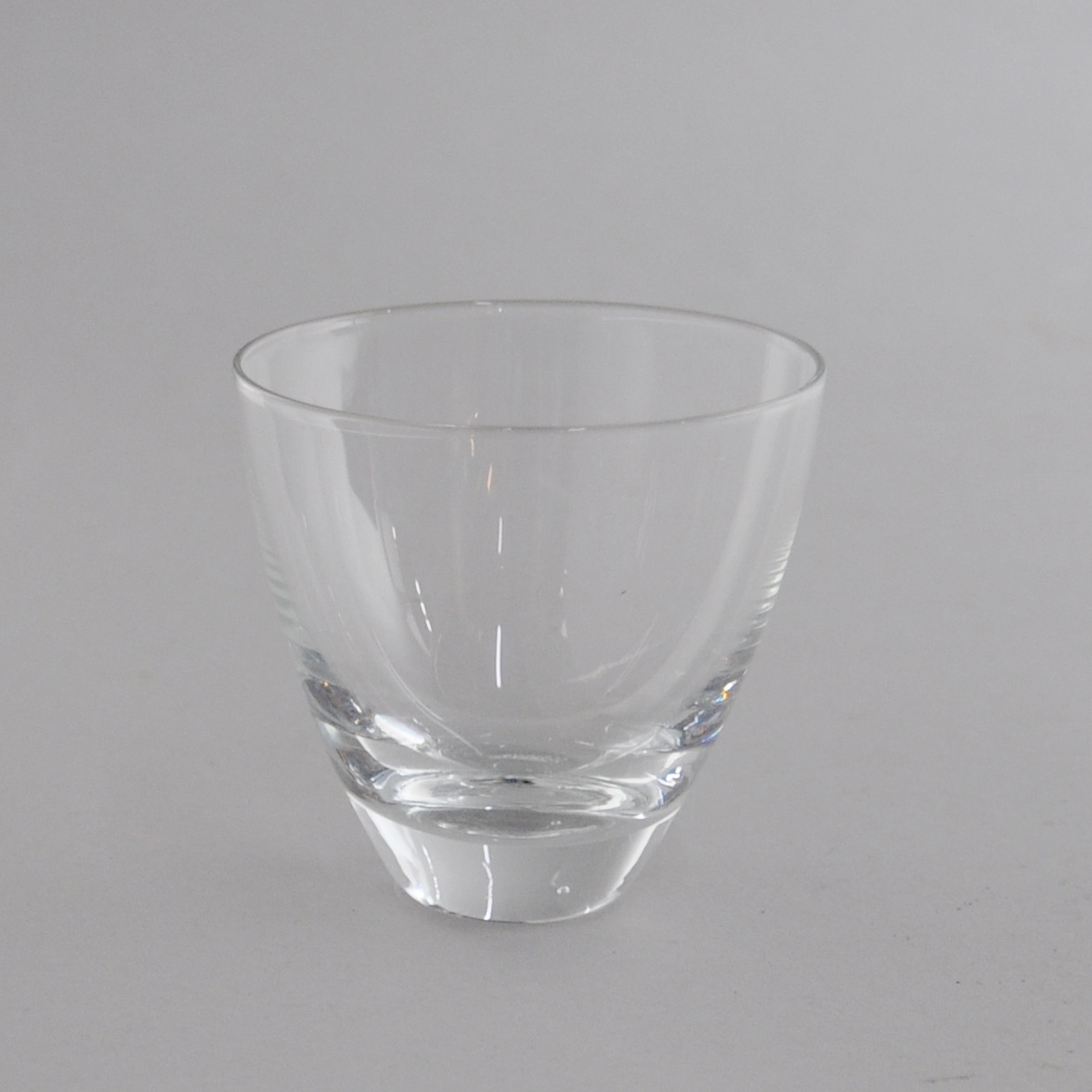 Glass til drikke. Glasset har utadgående kurvet form, med tykk bunn.