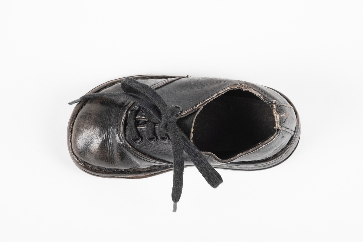 Et randsydd barnesko (høyre sko) av lær. Skoen har snøring med flate lisser. Maljene er av metall. Sålen er av lær og er forsterket med spiker på hælen og ved tuppen på undersiden.