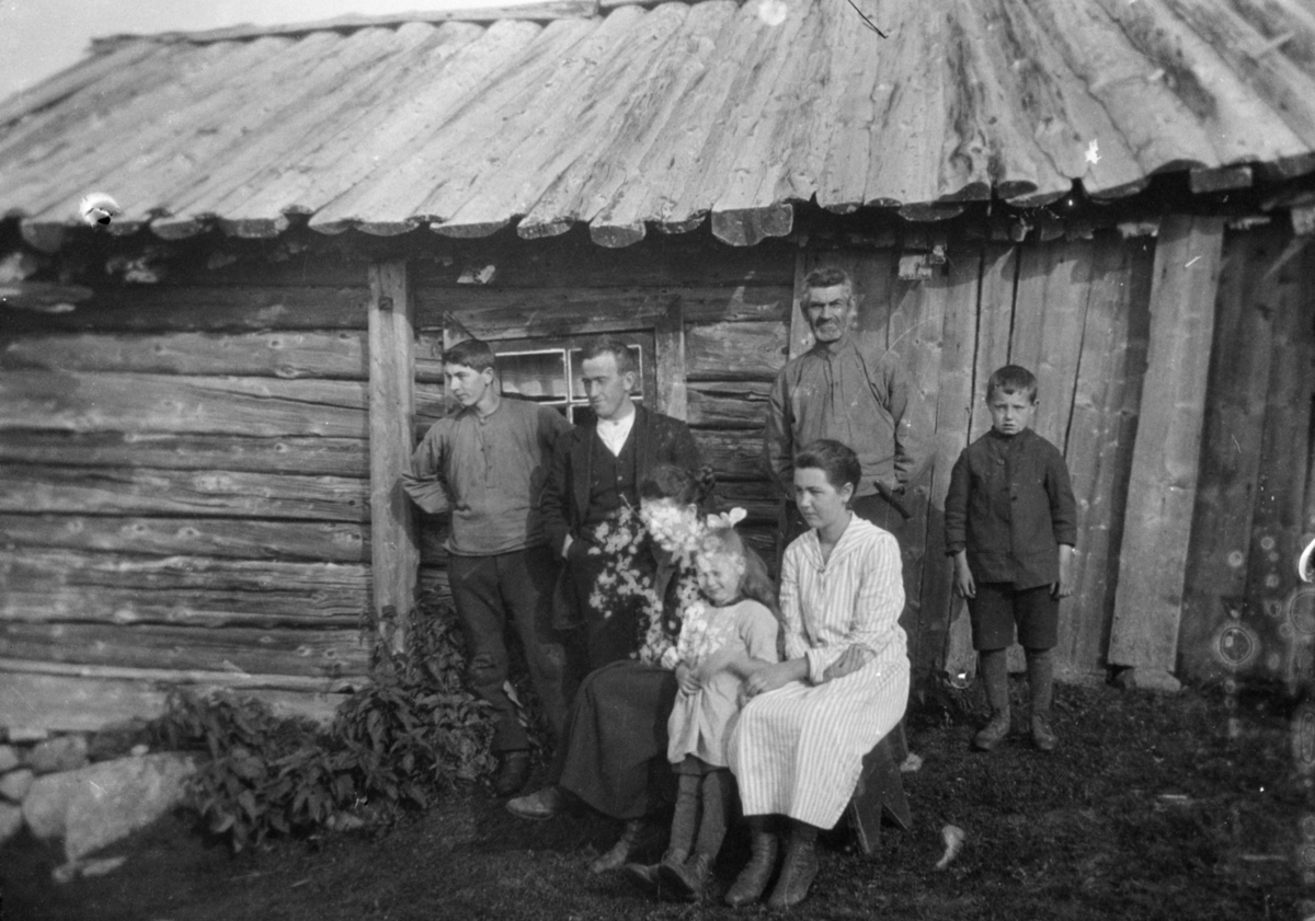 Fem voksne og to barn foran et seterhus eller ei hytte