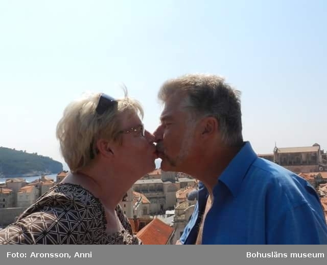 Anni och Kjell kysser varandra, bakom dem syns takåsar, en vik och skärgård.