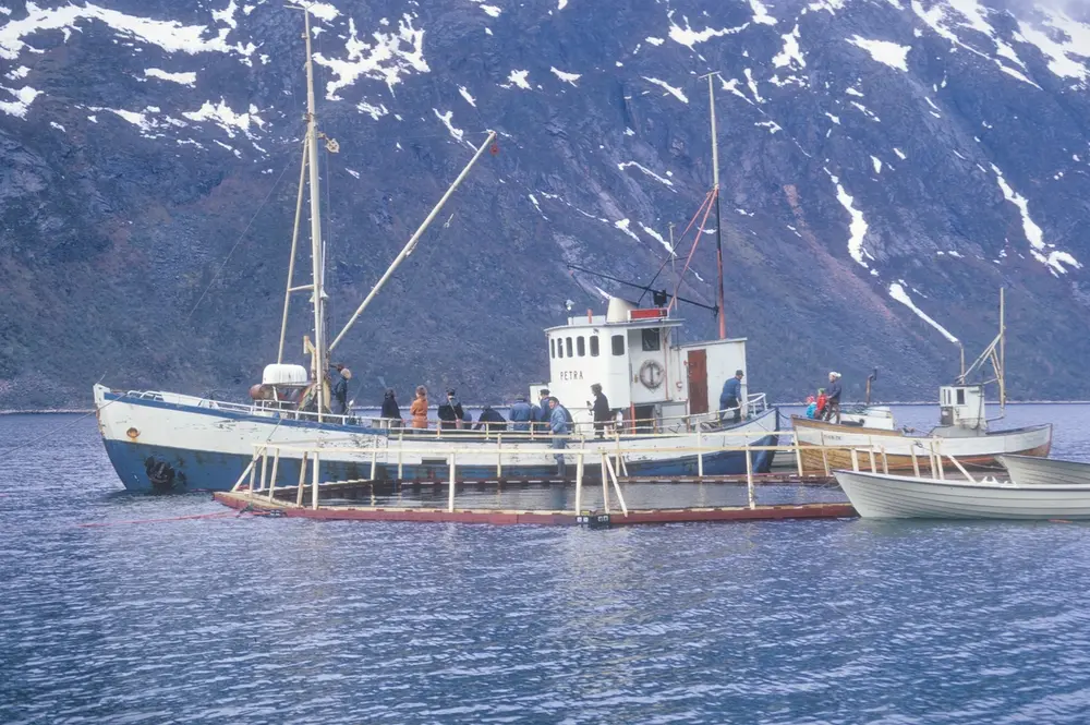 Flakstad fiskeoppdrett, 1974 : Brønnbåten "Petra" ligger ved en merde av typen "Grøntvedtmerde". Rundt dem ligger det flere små båter. Den mindre fiskebåten tilhørte røkteren på anlegget.