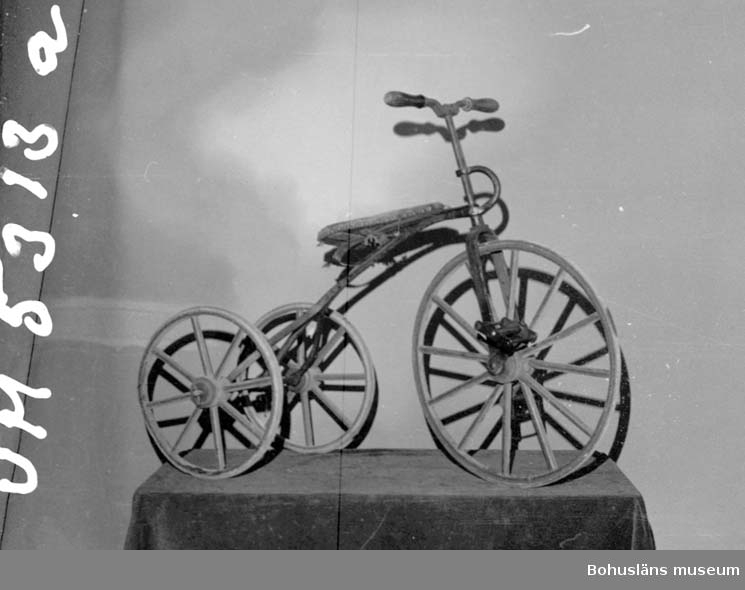 Ur handskrivna katalogen 1957-1958:
Trehjulig barncykel, Danmark 1885
L. 103, H. c:a 78 cm; järnram, hjul av trä m. järnringar; stoppad sits, klädd m. läder; a) rödmålad. Sitsens fäste trasigt, f.ö. hel. b) Åksäte m. fotstöd, tillhör cykeln; H. 41; 41; Br. 32 cm; järnram, trä t. sits och fotstöd; brunmålat. Ngt rost. Helt.

Lappkatalog: 40
