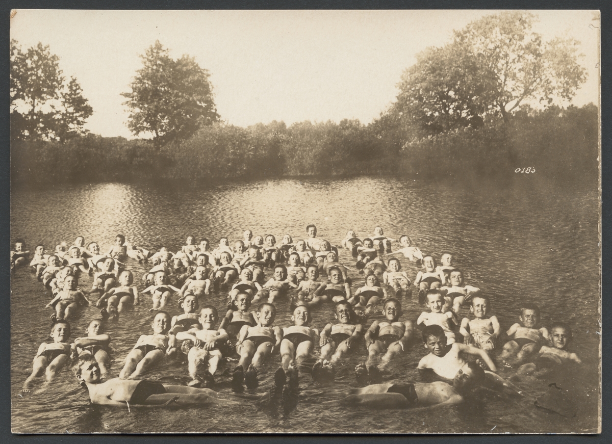 Bilden visar en större grupp badande pojkar i floden Bober i Schlesien.  Pojkarna ligger på ryggen i grund vatten.