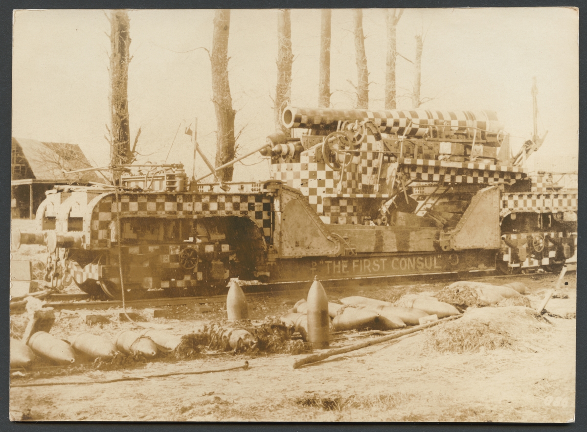 Bilden visar en engelsk järnvägsartilleripjäs med maskeringsmålning. Kanonen är döpt till namnen "The first consul". I förgrunden ligger en rad granater.