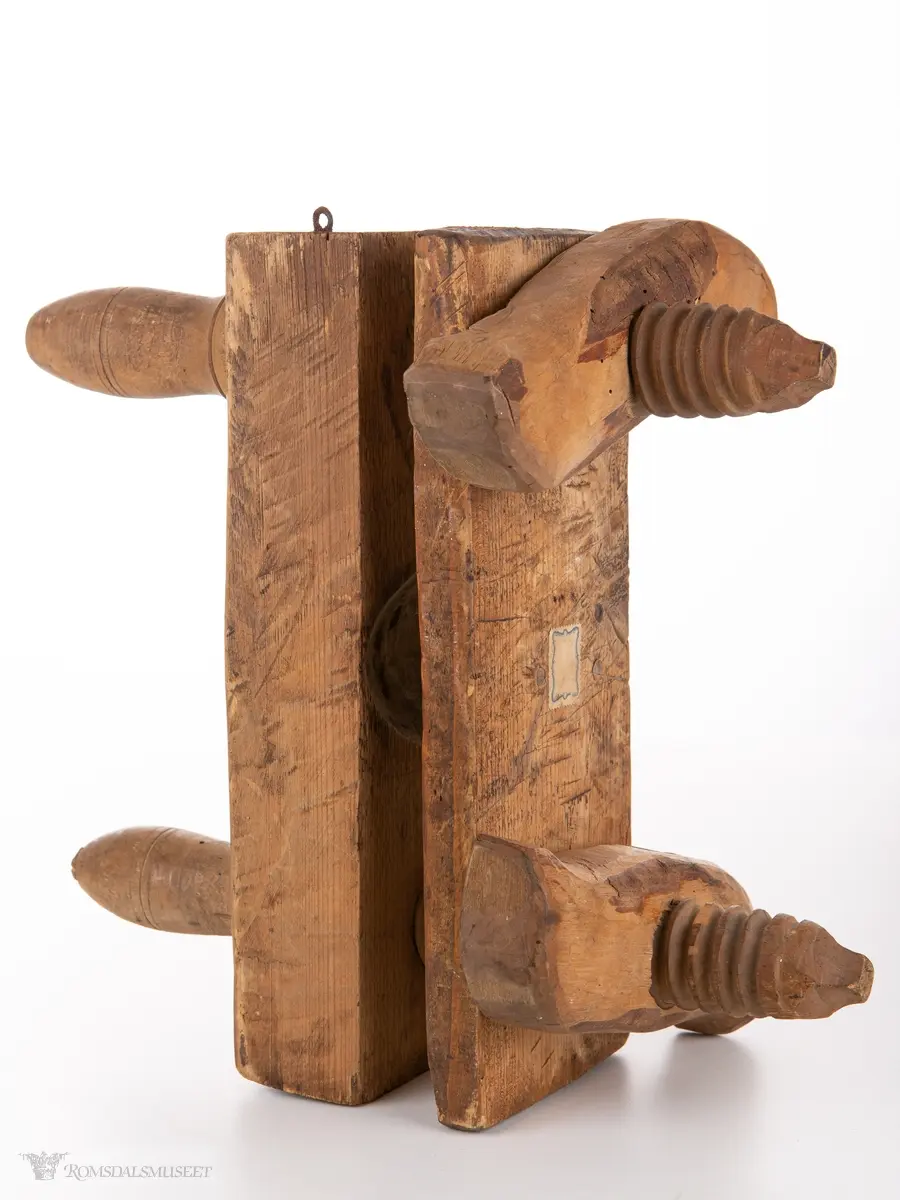 Treblokk med konkav skeiform og et motstyke med konveks skeiform. Disse er forbundet med dreide strammeskruer med låsestykker.