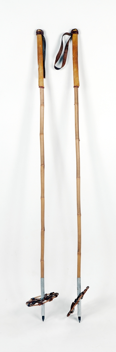 Ett par skidstavar av bambu med holk av lättmetall och järndubb, rottingkringla med korslagda läderremmar fästa vid en metallring. Greppet lindat med läder, handrem av läder nitad med kopparstift.