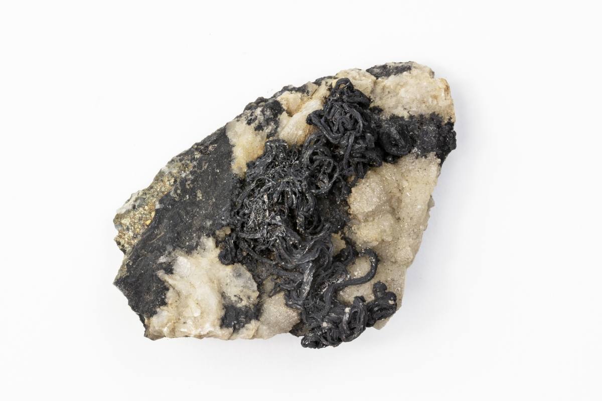 Ett mineral av ett grundämne. Detta mineral består av gediget silver i trådform. Det är det svarta på exemplaret som är silvret. Exemplaret kommer ifrån dåvarande Böhmen i Österrike-Ungern och ingår i Adolf Andersohns samling.