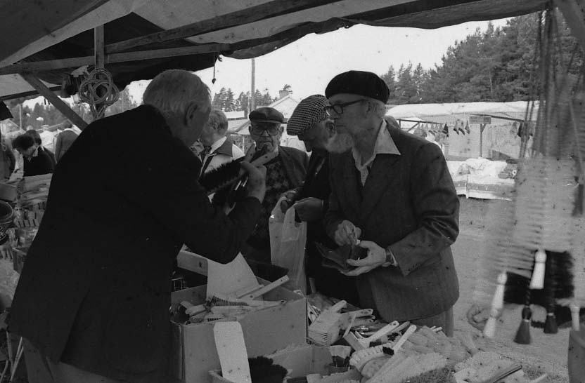 Ett marknadsstånd i Adelöv med borstar av olika sorter. Mannen närmast i bild med basker på huvudet är Gustav Johansson, som står i begrepp att handla.