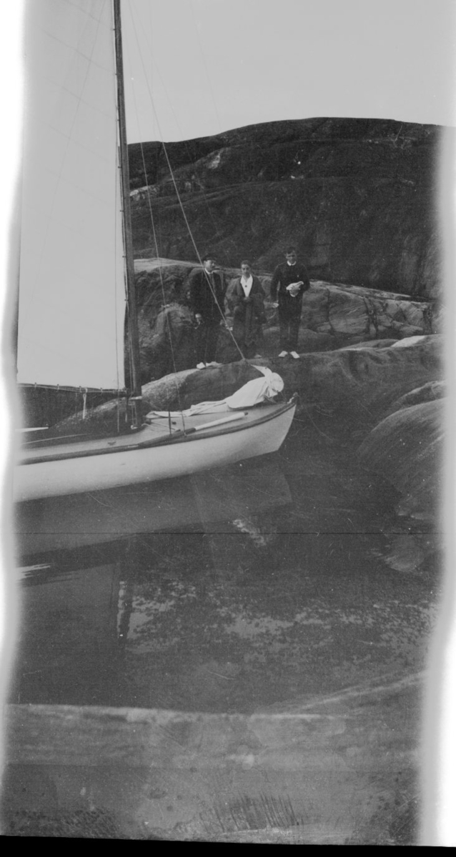Mann, kvinne og barn står på svaberg. Seilbåten ligger ved.  Ca. 1920 - 30